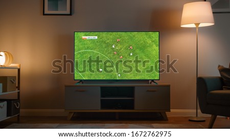 Shot of a TV with Soccer Match. Cozy Evening Living Room with a Chair and Lamps Turned On at Home. Royalty-Free Stock Photo #1672762975