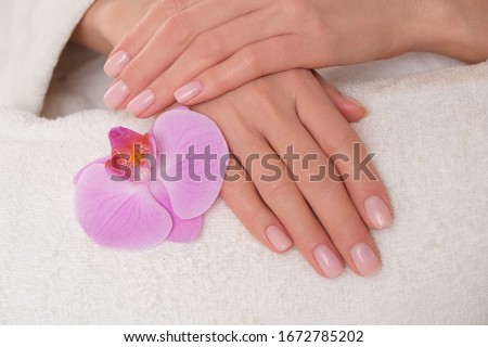 Beautiful delicate manicure on female hands. The picture of hands lying on the white towel with purple orchid.