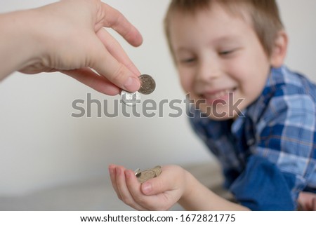 A happy boy receives coins from his mother's hands. The child is happy, smiling. Pocket money for a preschooler.Selective focus, blurred background. Close-up photo, cropped. Royalty-Free Stock Photo #1672821775
