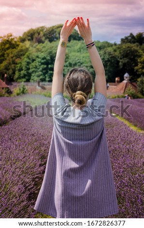 Young girl enjoying the view of the beautiful lavender garden raising her hands up to the sky