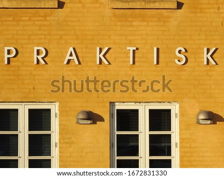 Details from a yellow   facade with letters saying "praktisk", Danish for "practical"    