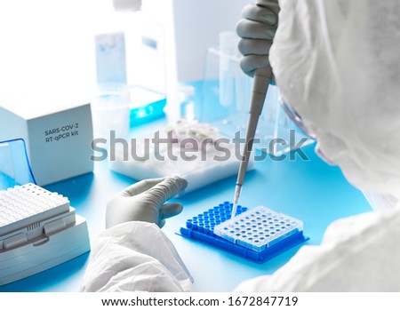 Tech in protective suit, mask and glasses works with patient swabs to detect specific region of 2019-nCoV virus causing Covid-19 viral pneumonia. SARS-COV-2 pcr diagnostics kit concept. Royalty-Free Stock Photo #1672847719