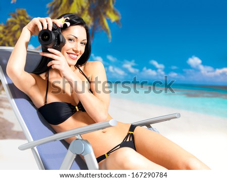Happy woman with a digital camera taking photos on the beach