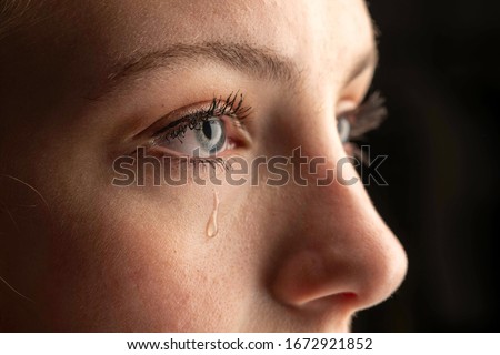 closeup photo of a young woman crying with a tear running down her cheek. Royalty-Free Stock Photo #1672921852