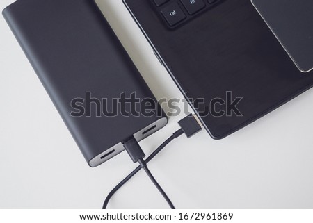 An open laptop is charged using a power bank via a cable. Portable modern devices. External battery, cable, USB and laptop, close-up.