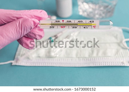 doctors hand in pink latex glove holding thermometer indicating high temperature. Healthcare and medicine concept.