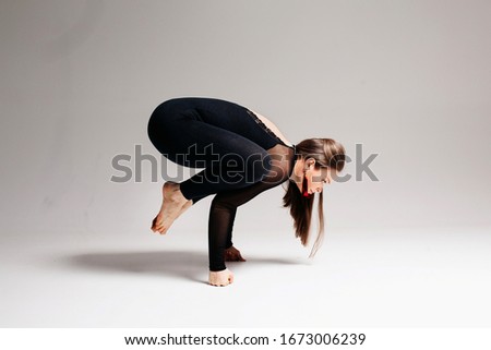 A beautiful girl of European appearance brunette sits in a difficult pose from yoga. She stands on her hands in fists, balancing. Photo on a white background.