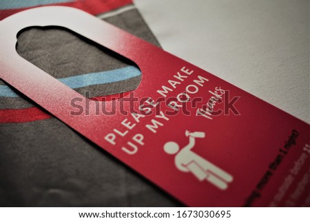 A close up image of a generic "Please make up my room" red door hanger for a hotel. Nice detail on the hanger, with focus on the type and graphic being shown. The hotel bed is in the background.