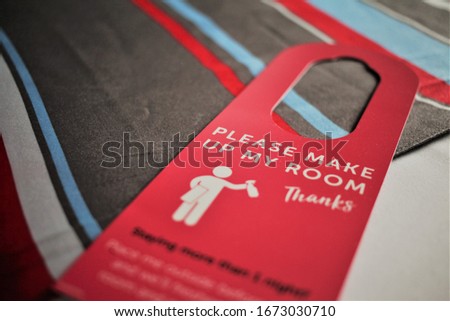 A close up image of a generic "Please make up my room" red door hanger for a hotel. Nice detail on the hanger, with focus on the type and graphic being shown. The hotel bed is in the background.