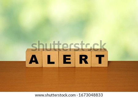 ALERT message word on a wooden desk on cube blocks with a green nature background
