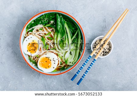 Asian Udon or Ramen noodles miso soup in bowl with Bok Choy and boiled egg on grey stone background. Top view, copy space.