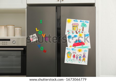 Modern refrigerator with child's drawings, note and magnets in kitchen