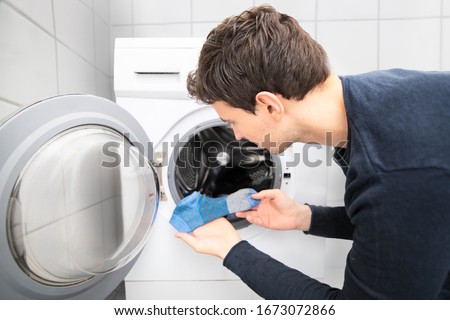 man looking for missing socks in washing mashine and found only one blue sock Royalty-Free Stock Photo #1673072866