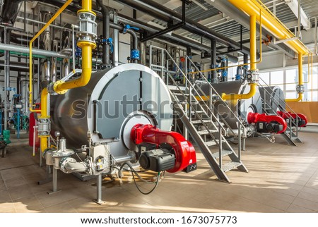 The interior of an industrial boiler room with three large boilers, many pipes, valves and sensors. Royalty-Free Stock Photo #1673075773