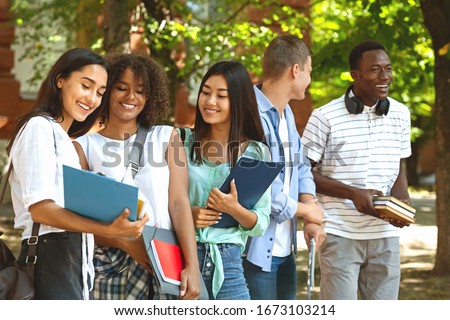 Group of international students resting in campus outdoors during break in classes, chatting and smiling Royalty-Free Stock Photo #1673103214