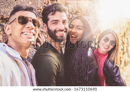 Portrait of a group of young multiracial people having fun taking a selfie with their smartphones. Millennial people outdoors taking self portraits using new technologies in a sunny day.