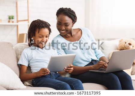 Technology Concept. Happy black family sitting on sofa, using laptop and digital tablet at home, free space