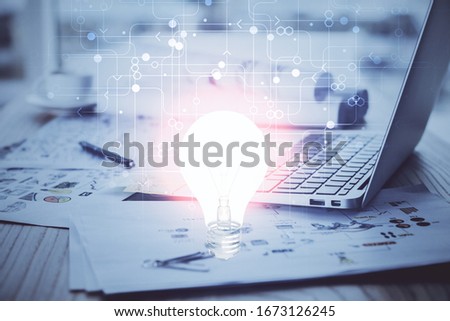 Computer on desktop in office with bulb icon hologram. Multi exposure. Concept of idea.
