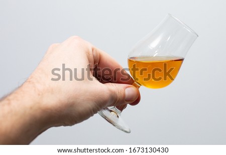 close-up of  whiskey tasting glass with whiskey held in a hand on a gray background