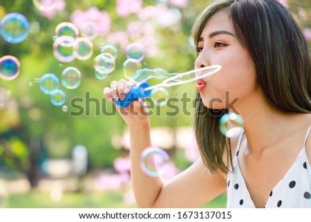 Outdoor autumn summer portrait of asian young beautiful happy woman making soap bubbles in park. Her Joyous happy in white dress. Holiday relaxation ideas