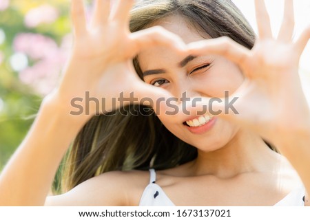 Outdoor autumn summer. Portrait of a asian young beautiful Holding Heart Shaped Hands Near Eyes Show love. Close Up shots of smiling faces and good skin health. Royalty-Free Stock Photo #1673137021