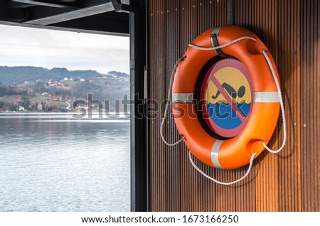 Lifebuoy hanging by the lake. Sign prohibiting swimming in water. Drowning hazard. Forbidden swimming in the see or lake. 