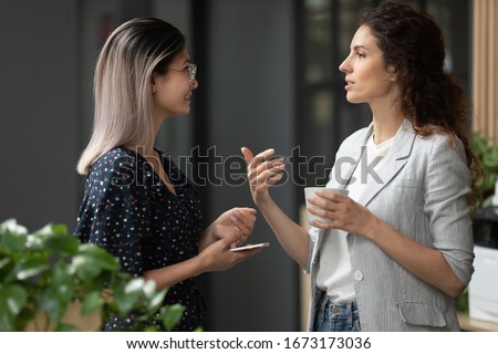 Smiling diverse employees chatting, discussing work during coffee break in office, Asian businesswoman wearing glasses listening to colleague, having pleasant conversation, good friendly relationship Royalty-Free Stock Photo #1673173036