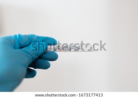 Medical thermometer being held by hand with protective blue rubber glove. Isolated against white background. 