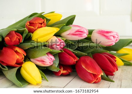 A bouquet of multicolored tulips lies on a white wooden background, side view