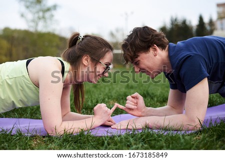 Young couple in love, doing sport exercises together. Brunette woman in eyeglasses, standing in plank together with curly man, looking at each other, smiling, laughing, holding hands. Active lifestyle