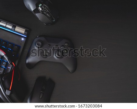 gamer workspace concept, top view a gaming gear, mouse, keyboard, joystick, headset, in ear headphone and mouse pad on black table background.