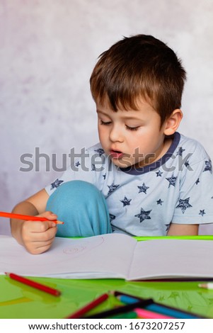 Little boy drawing with color pencils. Little boy is holding color pencils. Boy, drawing a picture for fathers day. Small boy draws at the table.