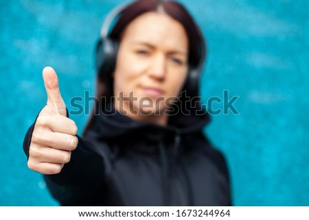 Young female in blur showing  thumb up on blue background