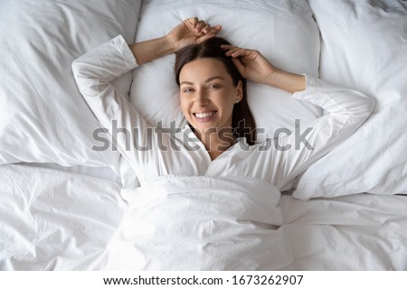 Above top view head shot young smiling lady lying on comfortable mattress soft pillow under duvet, looking at camera. Happy brunette woman waking up, enjoying good morning time alone in bed. Royalty-Free Stock Photo #1673262907
