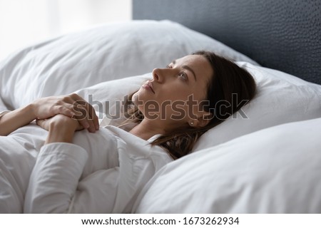 Side view head shot tired unhappy young woman lying in bed under blanket with opened eyes, suffering from insomnia. Stressed brunette lady resting in bed without sleep, thinking of personal problems. Royalty-Free Stock Photo #1673262934