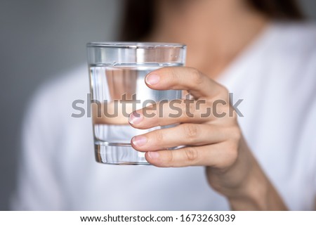 Close up focus on glass of pure distilled water in female hands. Young thirsty woman holding clear liquid aqua, ready drink, prevent organism from dehydration, body balance, healthcare, refreshment. Royalty-Free Stock Photo #1673263039