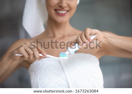 Cropped image young smiling woman putting whitening paste on toothbrush, starting cleaning teeth in morning. Happy lady taking care of gums health, preventing caries, healthy daily habit concept.