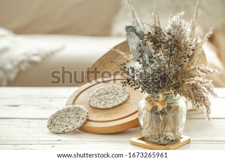 Decorative items in the cozy interior of the room , a vase with dried flowers on a light wooden table. Royalty-Free Stock Photo #1673265961