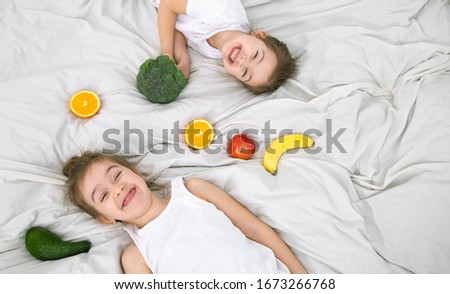 Happy two cute children play with fruits and vegetables on a light background . Healthy food for children .
