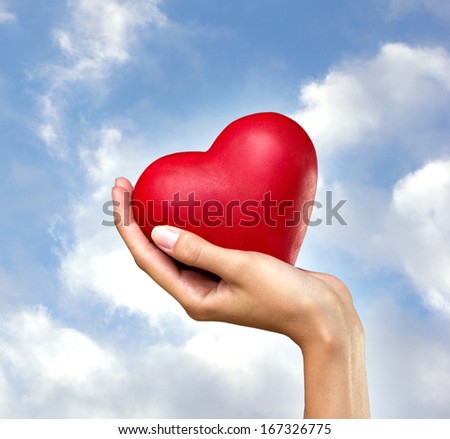 red heart in woman's hand on blue sky and clouds  background
