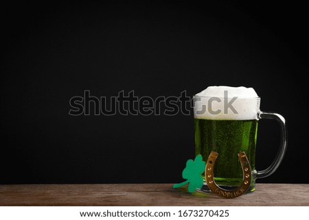 Green beer and clover on wooden table against black background, space for text. St. Patrick's Day celebration