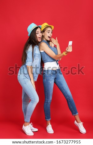 Young happy girlfriends making selfie on mobile phone on red background