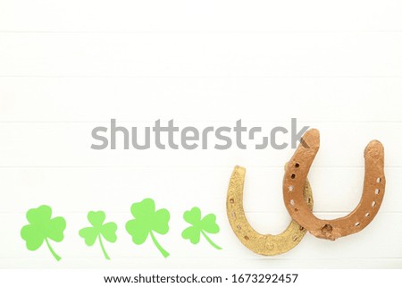 St.Patrick's Day. Paper clover leafs with golden horseshoes on white wooden table