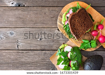 Healthy green sandwich with avocado, cucumber, spinach and radish. Top view side border against a rustic wood background. Copy space.