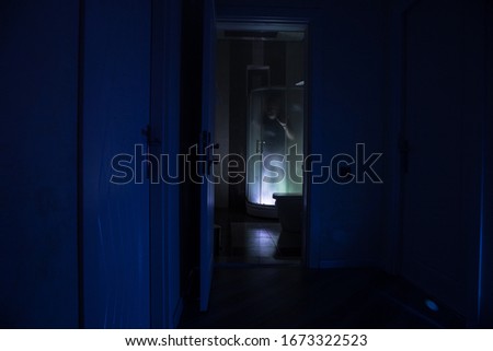 Halloween concept. Horror silhouette of person in shower cabin. Killer maniac inside bathroom with glowing lights. Long exposure