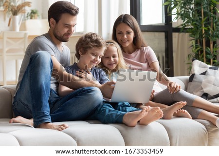 Happy young family with little kids sit on comfortable couch relaxing watching movie or cartoon on laptop together, overjoyed parents and small children enjoy funny video on computer at home