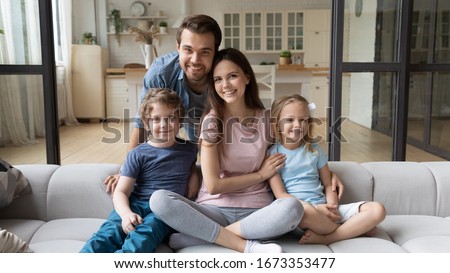 Portrait of happy successful young family with children first time home buyers sit on comfortable couch, smiling parents and little kids relax in living room look at camera posing, ownership concept