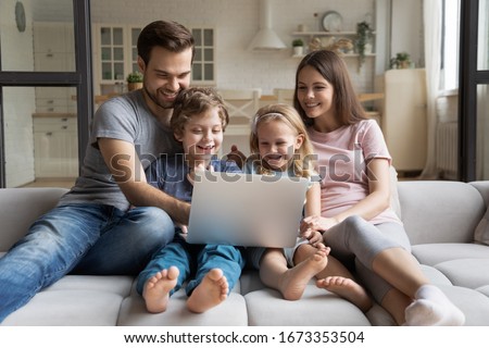 Overjoyed young family with small children sit relax on comfortable couch at home enjoying funny video on laptop, happy parents rest with kids on cozy sofa watching movie using computer together
