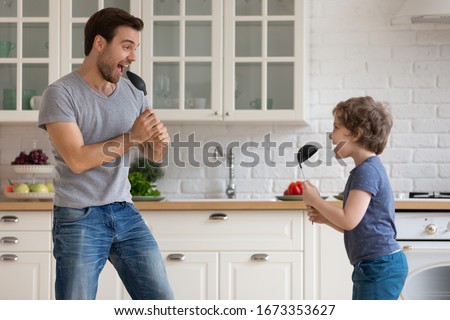 Overjoyed young father and little preschooler son have fun singing together using kitchen appliances, happy playful dad parent play with smiling excited small boy child entertain at home