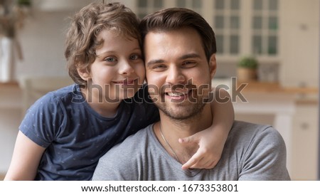 Close up portrait of smiling young father and preschooler son hug cuddle look at camera posing for family picture together, happy dad and cute little boy child embrace show support love and care